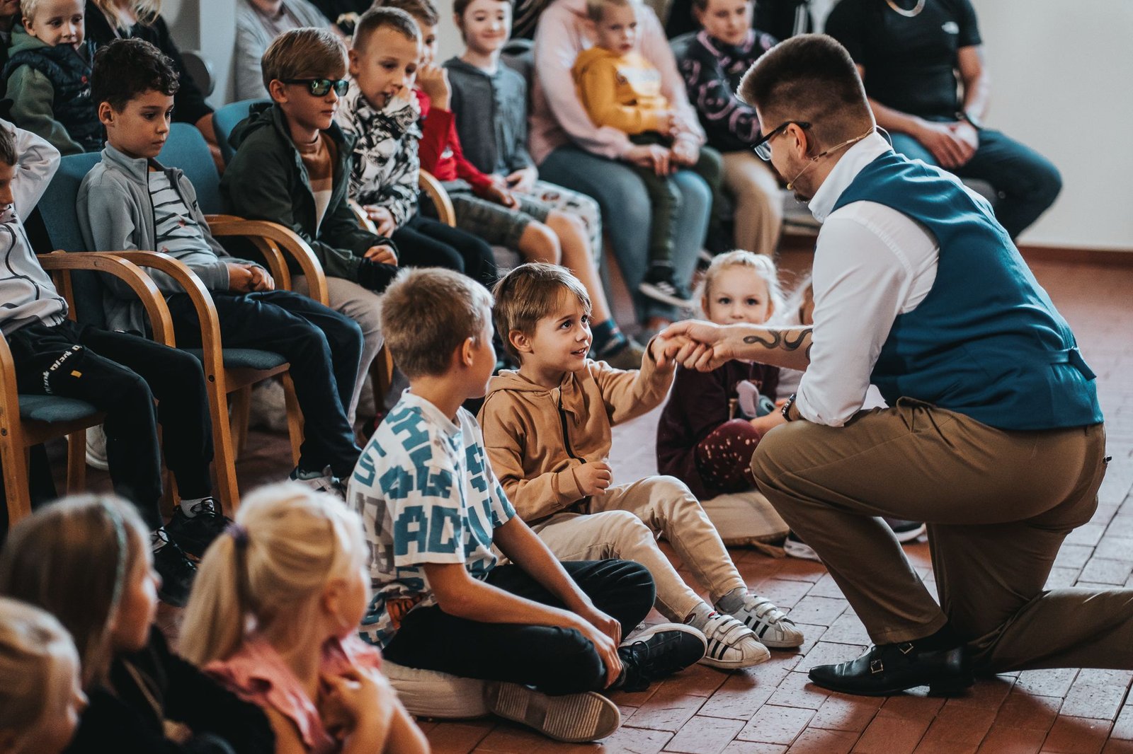 Iluzjonista dla dzieci Armand Górny kuca przy widowni i podaje rękę dziecku